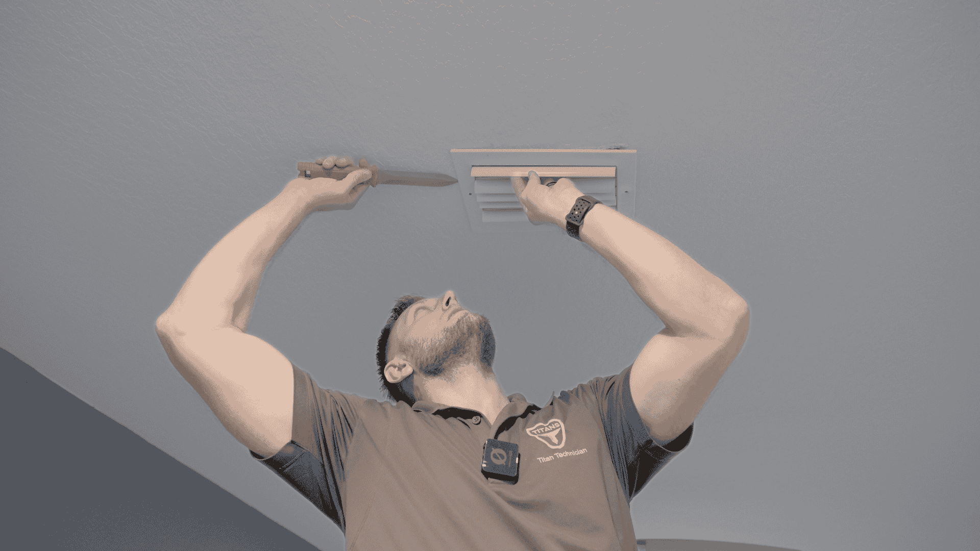 Air Titans technician on a ladder uses a screwdriver to remove a ceiling vent cover, preparing for an indoor air quality assessment.