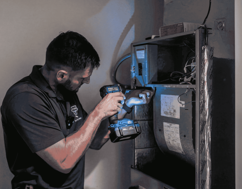 An Air Titans installer carries a large blower wheel out of an HVAC cabinet during a system installation.